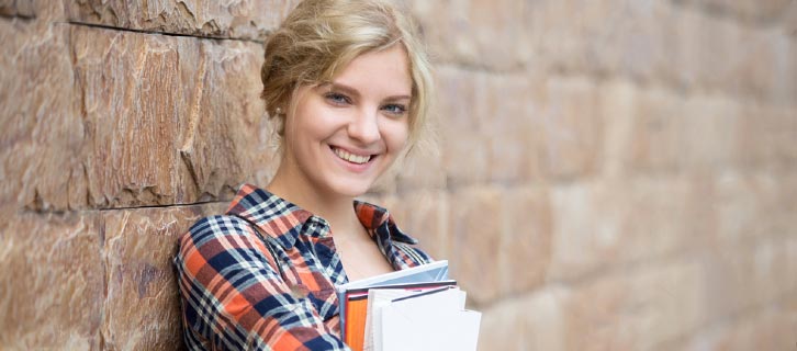 Auf Lehramt bewerben Fröhliche Lehramt-Studentin lächelt angelehnt an eine Wand.